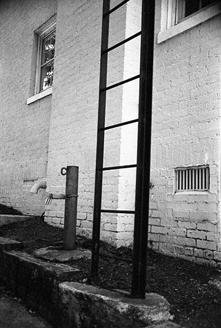 Exterior wall of old white brick building with metal ladder afixed to side (example of Phil's black and white photography)